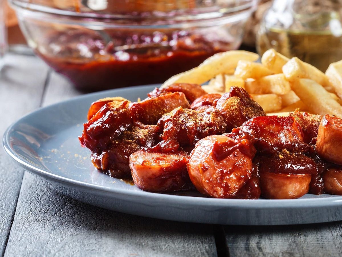 Ein Teller vegane Currywurst mit Sauce und Pommes.