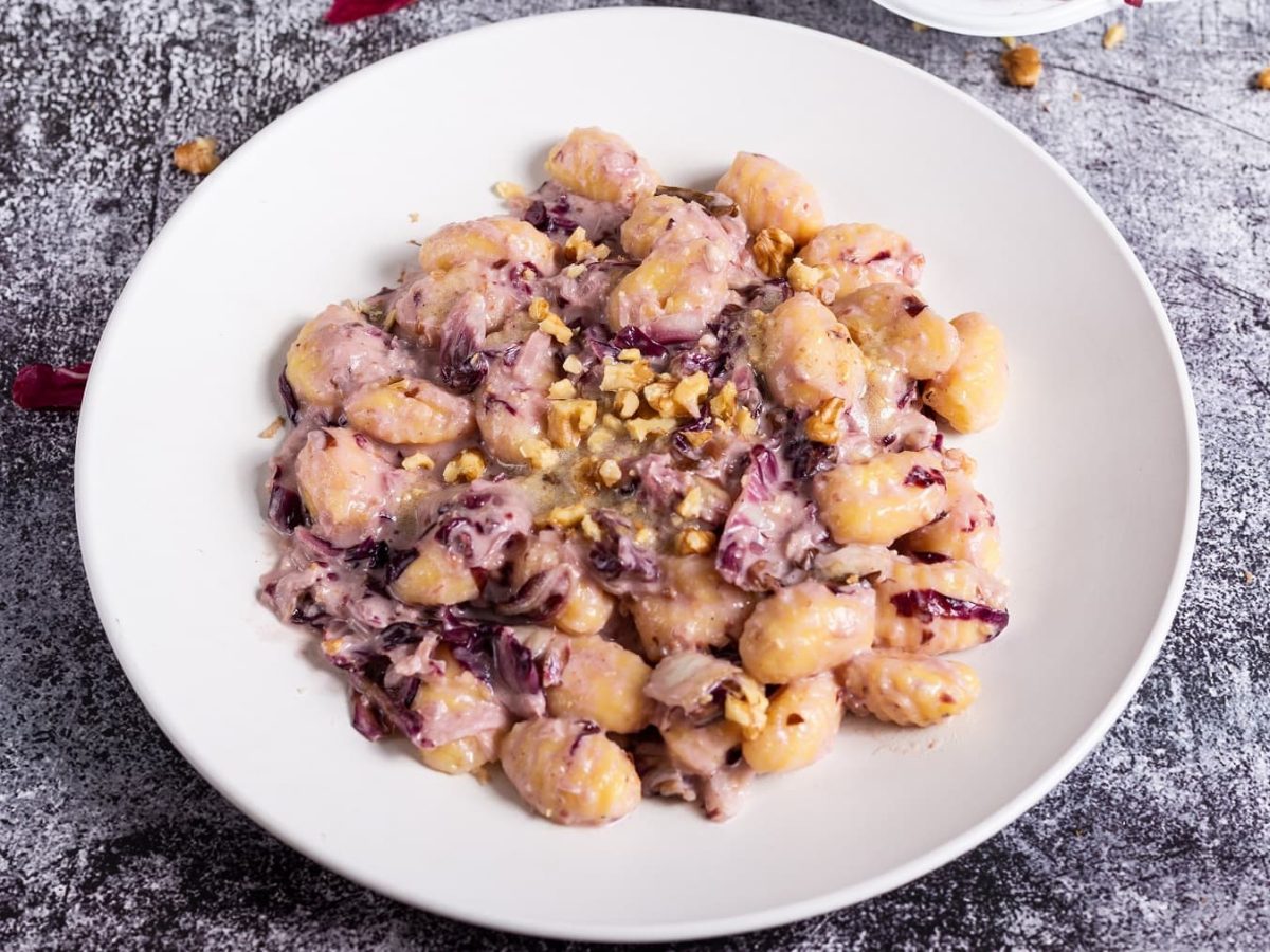 Ein Teller vegane Gnocchi mit Radicchio und Walnüssen auf schwarz-grauem Untergrund.