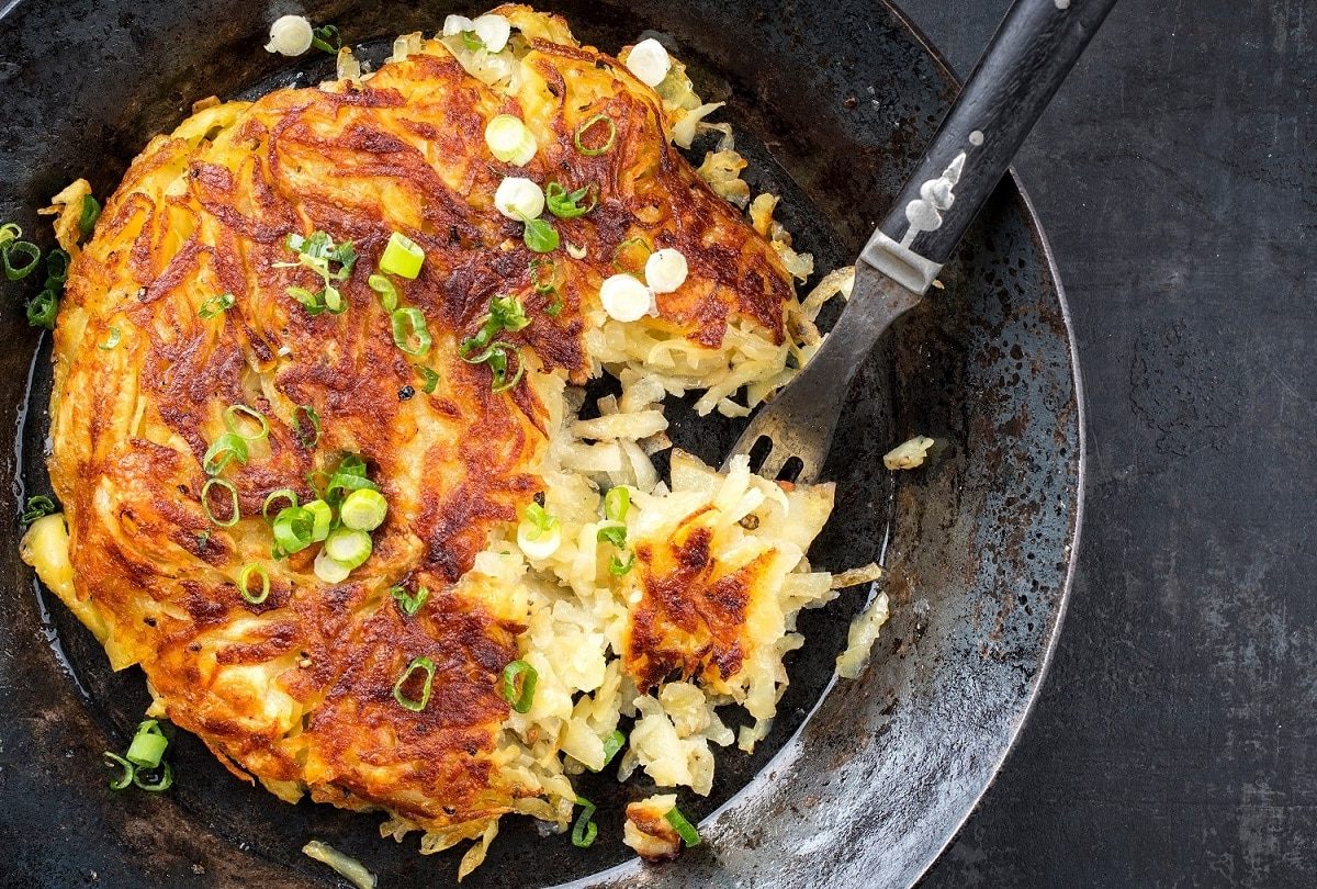 Eine gusseiserne Pfanne in der Draufsicht, darin ein veganer Kartoffelpuffer mit Lauch