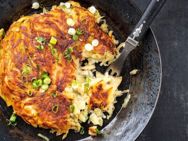 Eine gusseiserne Pfanne in der Draufsicht, darin ein veganer Kartoffelpuffer mit Lauch