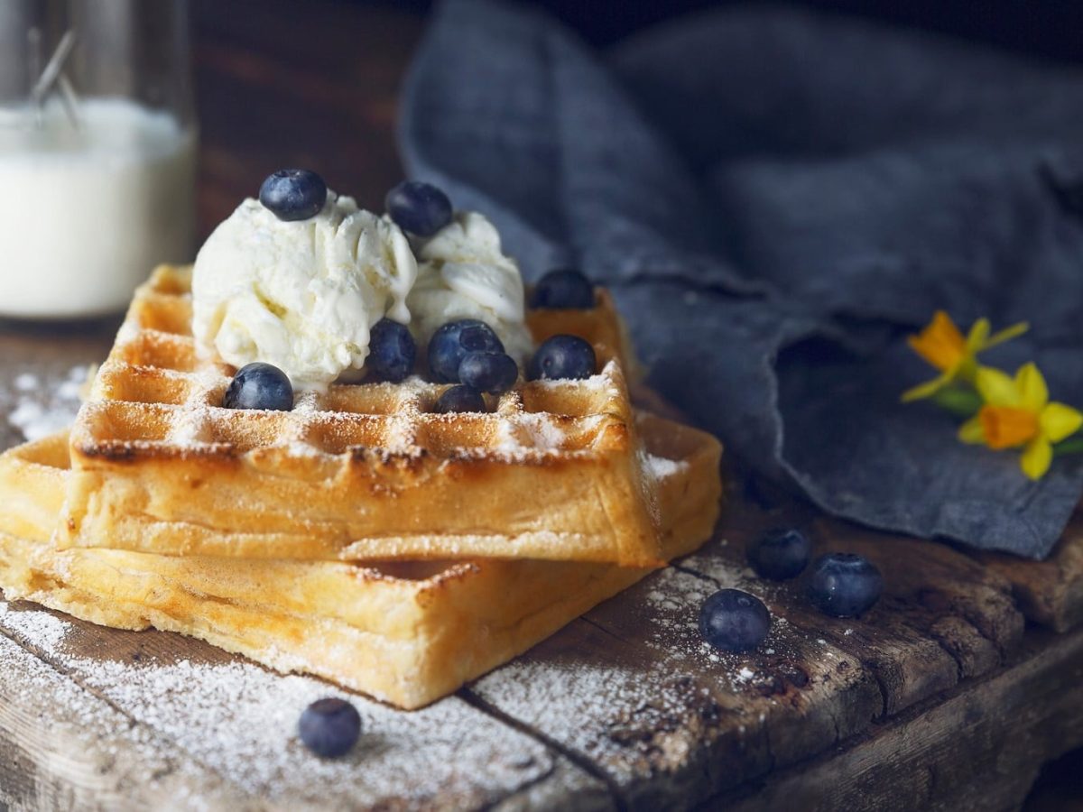 Zwei vegane Waffeln mit Blaubeeren und einer Kugel Vanilleeis auf rustikalem Holz.