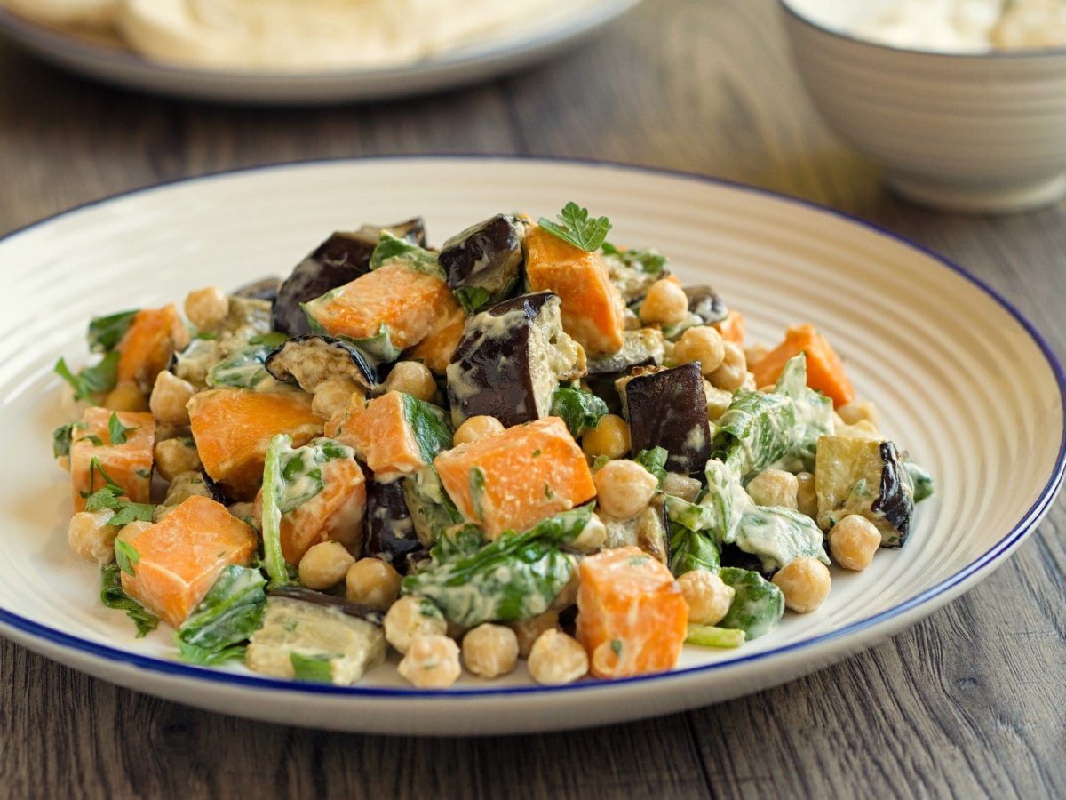 Ein Teller Veganer Kichererbsensalat mit Süßkartoffel, Aubergine und Spinat, daneben liegt eine Gabel.