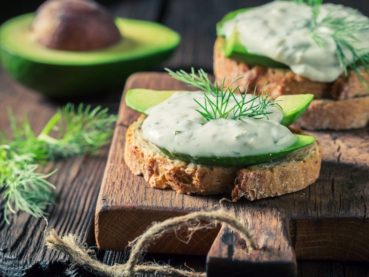 Baguettescheiben mit veganem Tzatziki mit Avocado auf einem rustikalen Holzbrett.