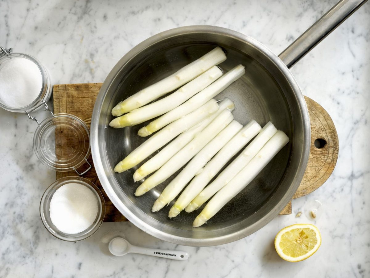 Weißer Spargel in einem Topf, daneben verschiedene Zutaten. Wie lange muss Spargel kochen?