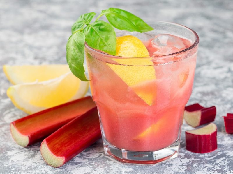 Ein rosa Drink mit Rhabarber und Zitrone auf grauem Steinuntergrund.