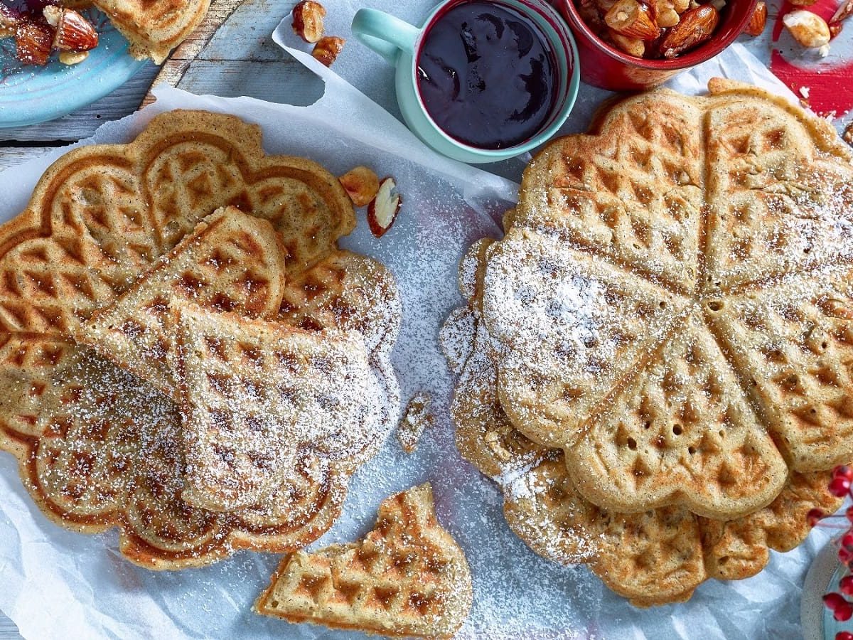 Auf einem Tisch liegen mehrere Herzwaffeln. Sie sind mit Puderzucker bestreut.