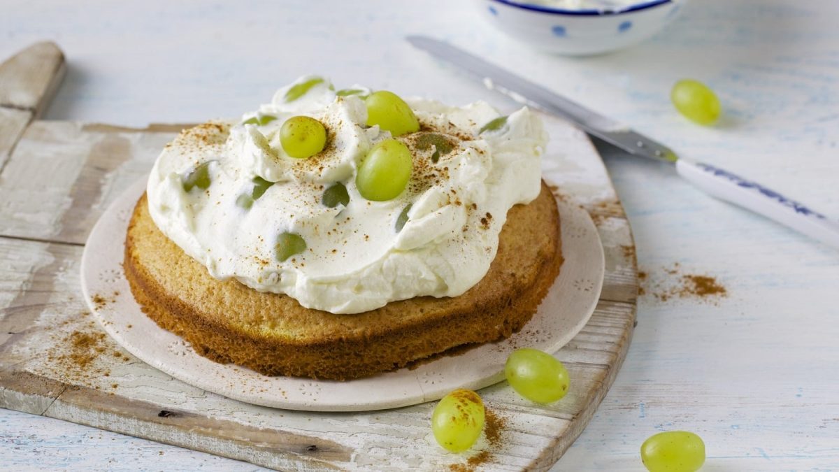 Auf einem Teller liegt ein Mini-Schmandkuchen mit Weintrauben. Die Creme ist fluffig und der Teig ist leicht.