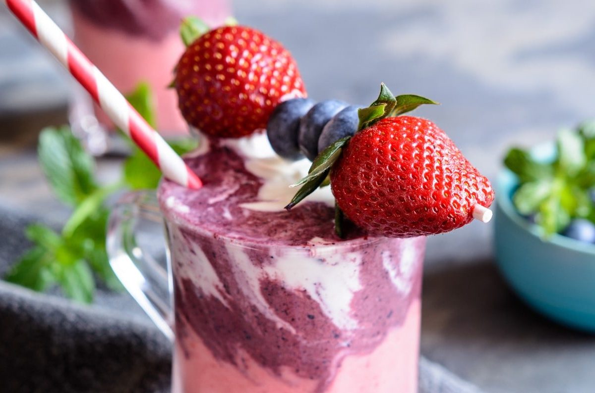 Erdbeer-Heidelbeer-Smoothie mit Joghurt mit frischen Früchten serviert.