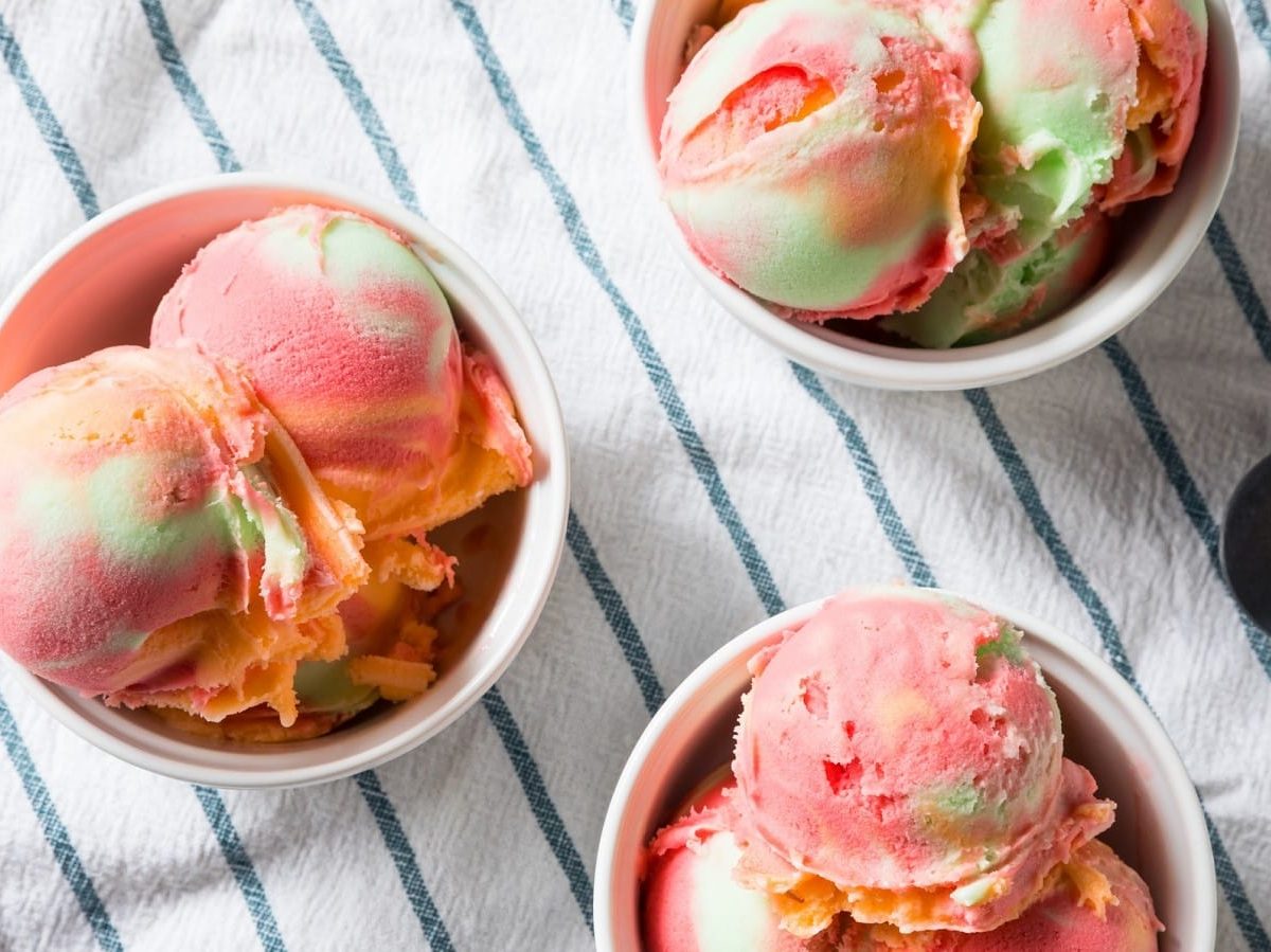 Regenbogen-Sorbet in drei Bechern auf einem gestreiften Küchentuch