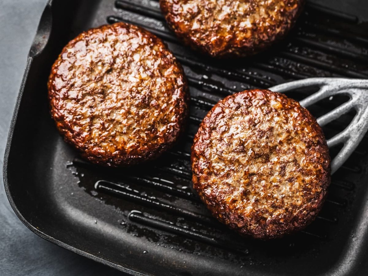 Drei gebratene Hackfleisch-Pattys in Grillpfanne.