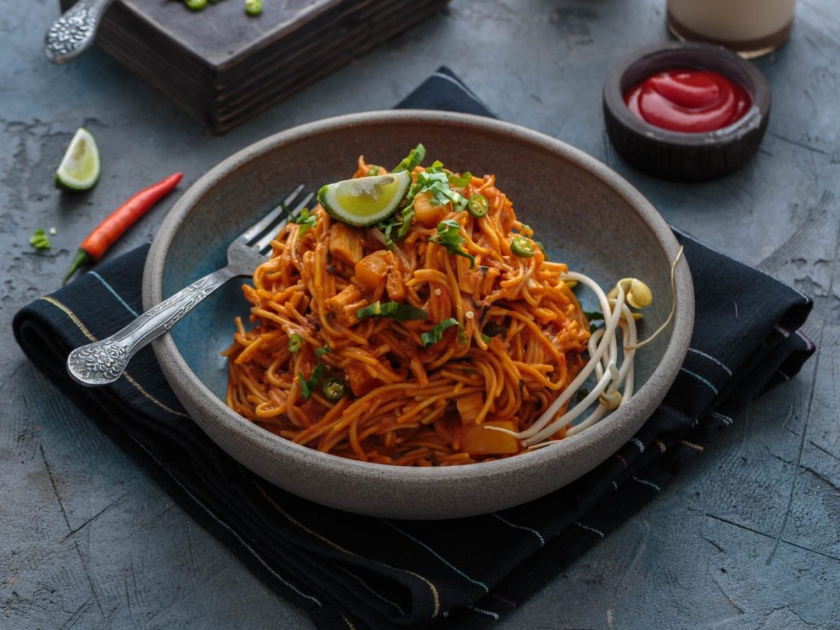 Mee Goreng Mamak in einer Schüssel auf einem Küchentuch. Im Hintergrund verschiedene Zutaten.