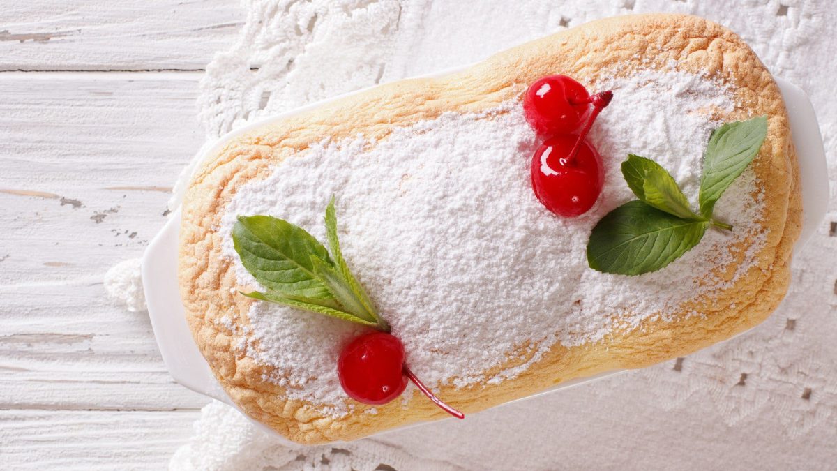 Salzburger Nockerln mit Puderzucker und Cocktailkirschen in weißer Form auf weißem Holz.