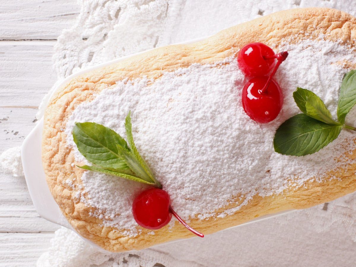 Salzburger Nockerln mit Puderzucker und Cocktailkirschen in weißer Form auf weißem Holz.