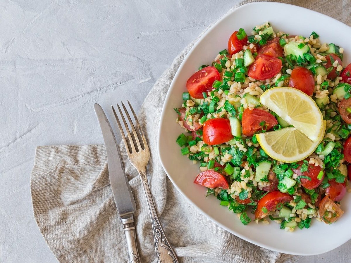 Auf einem teller ist ein schneller Bulgursalat mit Tomaten und Zitrone angerichtet.