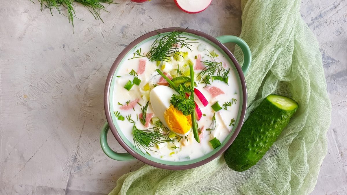 In einer Schüssel ist eine kalte Gurkensuppe angerichtet. Daneben liegt eine Gurke.