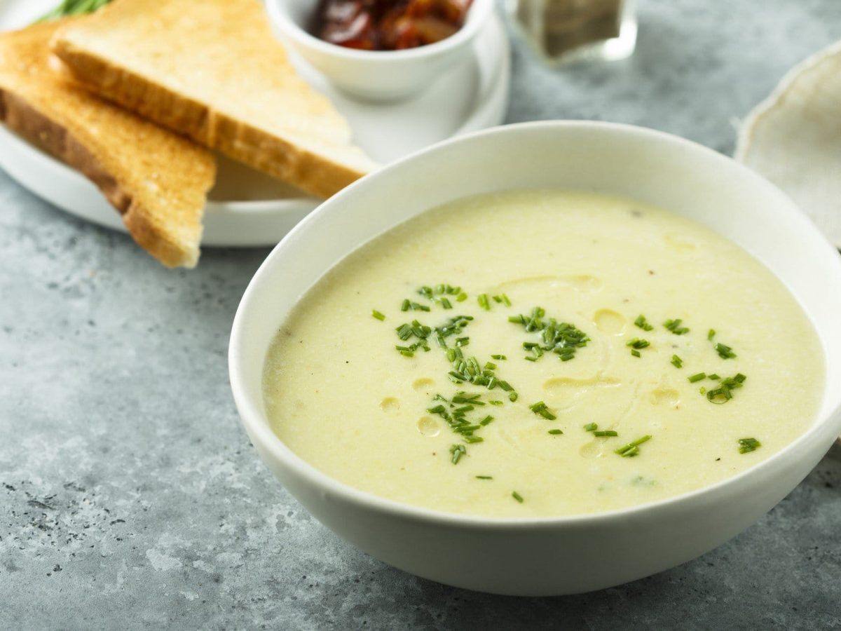 Spargelcremesuppe in einer weißen Schale. Im Hintergrund weitere Zutaten.