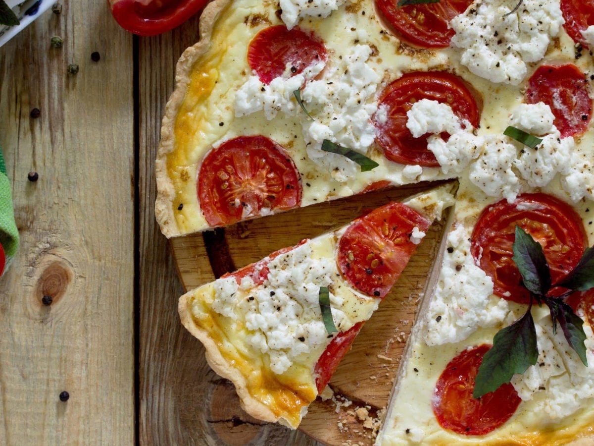 Tomaten-Ricotta-Quiche mit frischem Pfeffer auf hölzernem Untergrund.