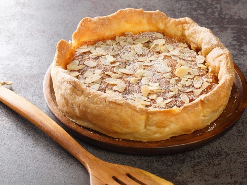 Ein Bakewell Pudding auf grauem Untergrund mit einem Holzkochlöffel.