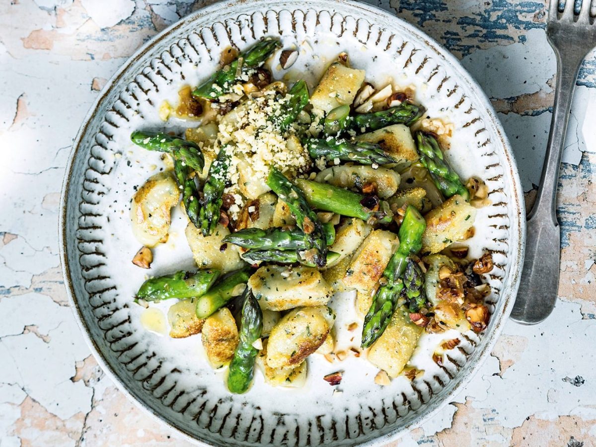 Ein Teller Basilikum-Gnocchi mit gebratenem grünem Spargel auf rustikalem Untergrund in der Draufsicht.