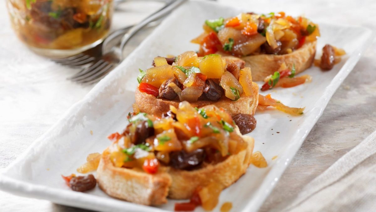 Drei Bruschetta mit Apfel-Ingwer-Chutney auf einer weißen Servierplatte.