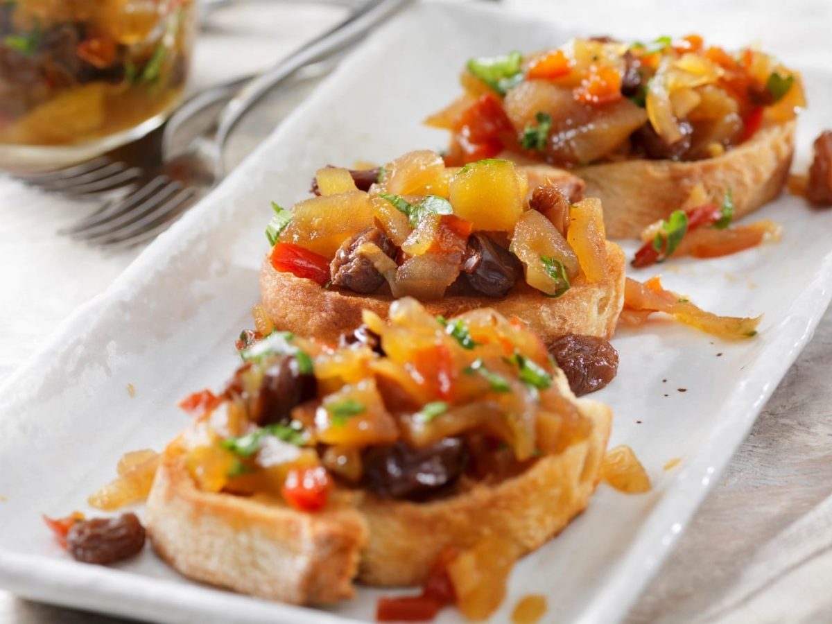 Drei Bruschetta mit Apfel-Ingwer-Chutney auf einer weißen Servierplatte.