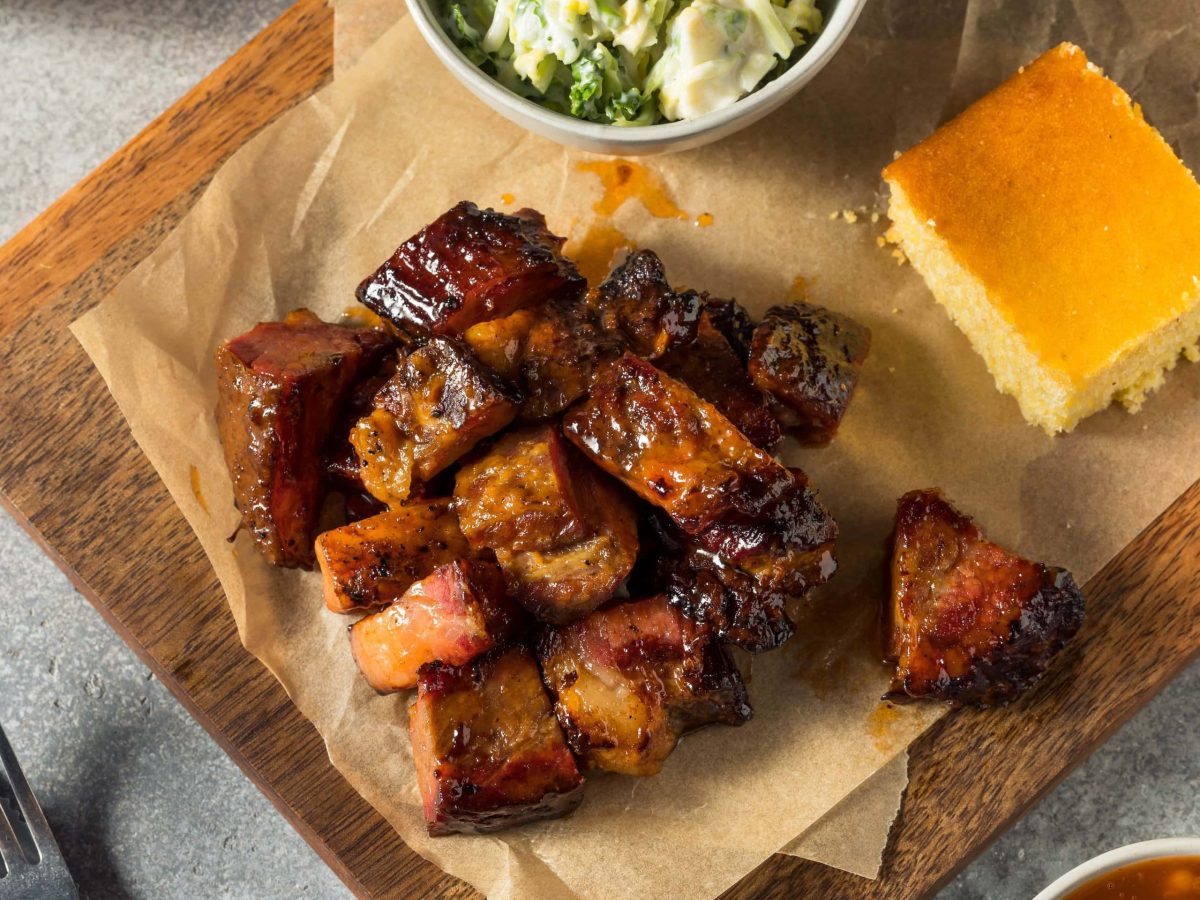 Burnt Ends mit allerhand Beilagen auf einem Holzbrett