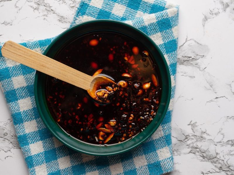 Ein Glas selbst gemachtes Sichuan-Chiliöl auf einem blau karierten Küchentuch