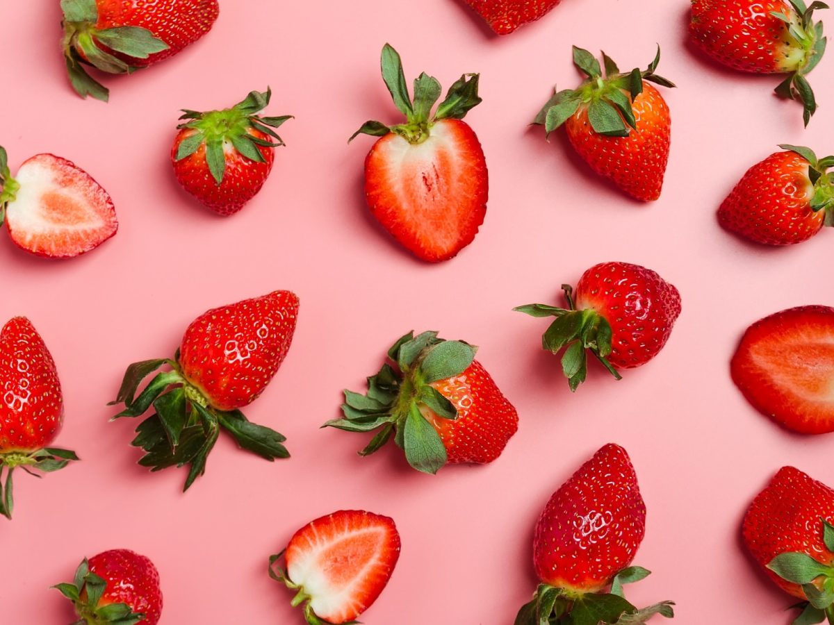 Auf einem rosa Hintergrunfd liegen Erdbeeren. manche sind halbiert.