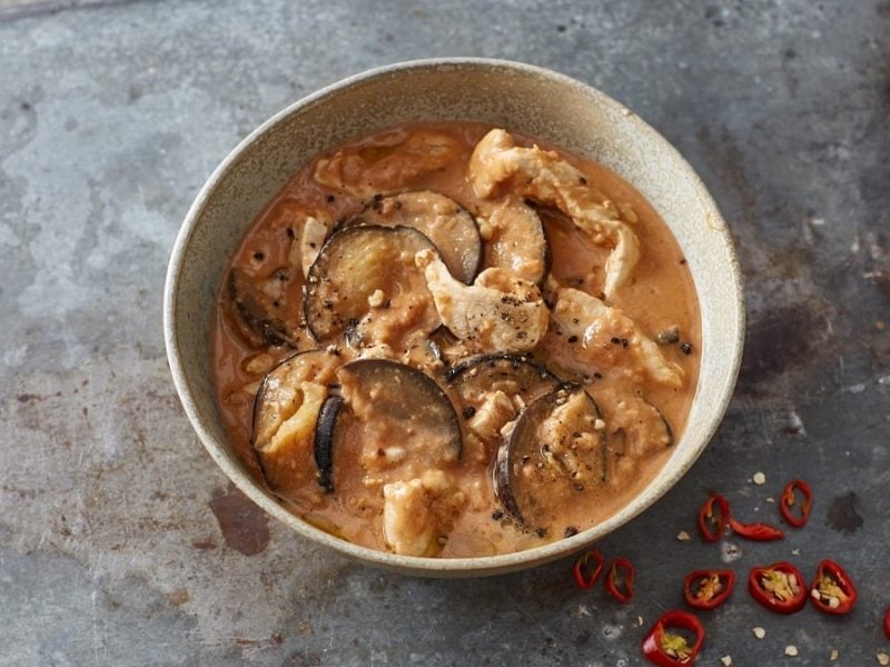 eine Schüssel mit einem Erdnuss-Hähnchen-Topf mit Aubergine steht auf einem Tisch. es handelt sich um ein Gericht aus Afrika.