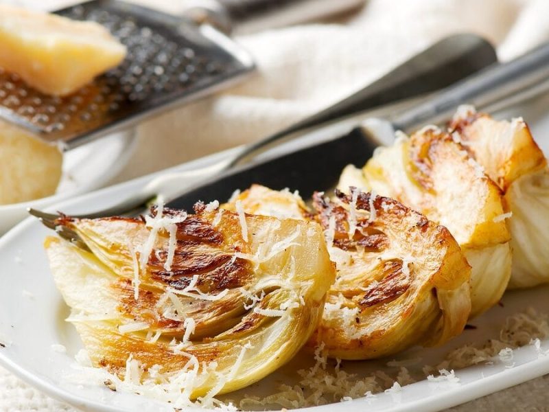 Auf einer Platte liegt gegrillter Fenchel, der mit Parmesan bestreut wurde.