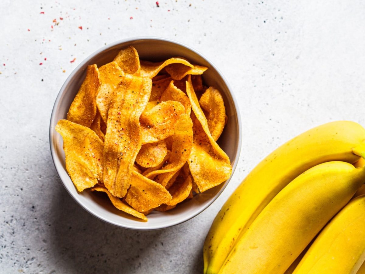 Herzhafte Bananenchips in einer weißen Schale. Daneben Bananen.