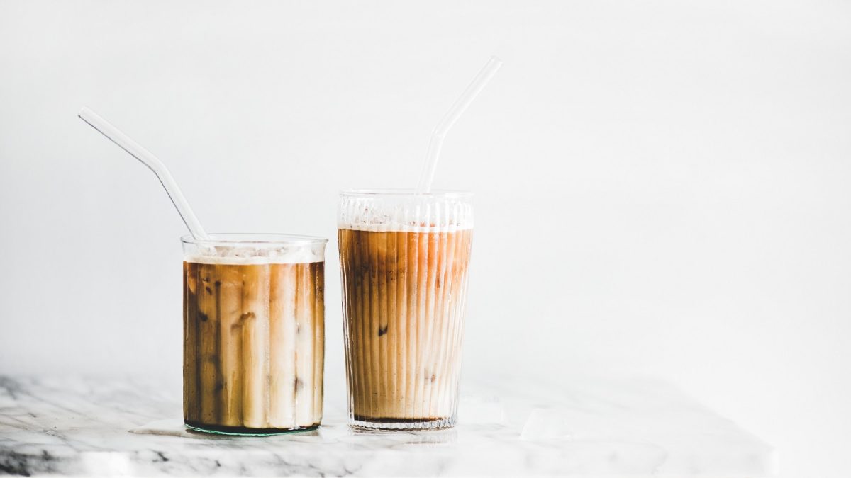 Zwei Gläser Iced Caramel Macchiato mit Strohhalmen auf einem weißen Marmortisch.