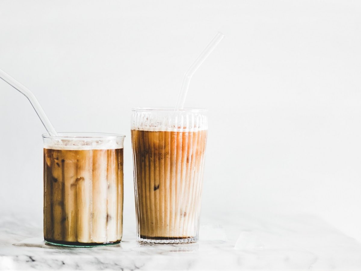 Zwei Gläser Iced Caramel Macchiato mit Strohhalmen auf einem weißen Marmortisch.