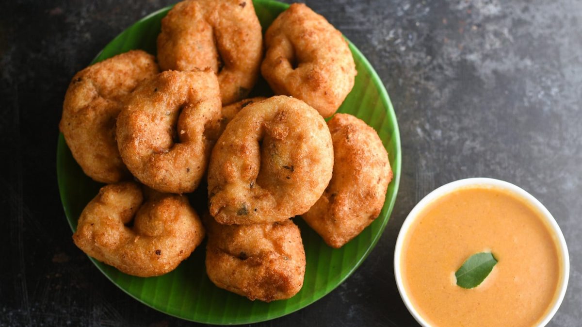 Medu Vada, ein indischer Snack auf einem grünen Teller neben einem Dip auf einem grauen Tisch