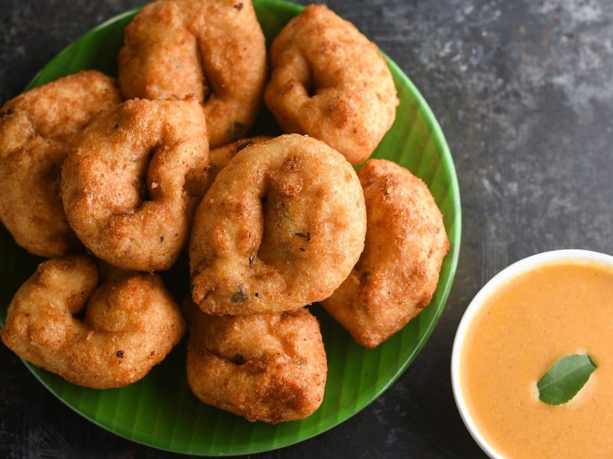 Medu Vada, ein indischer Snack auf einem grünen Teller neben einem Dip auf einem grauen Tisch