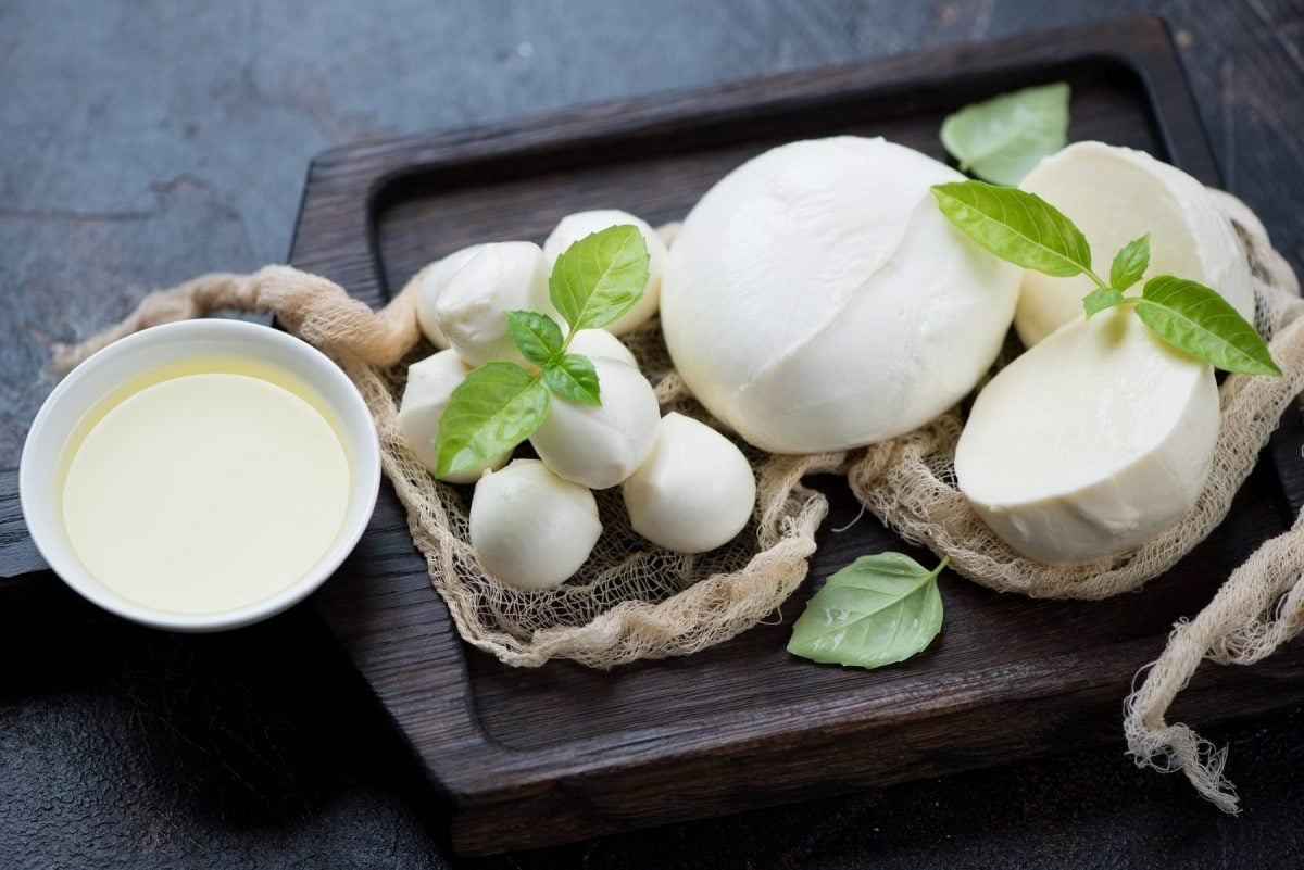 Mehrere Kugel Mozzarella liegen auf einem groben Tuch. daneben eine Schale mit Lake sowie Basilikumblätter.