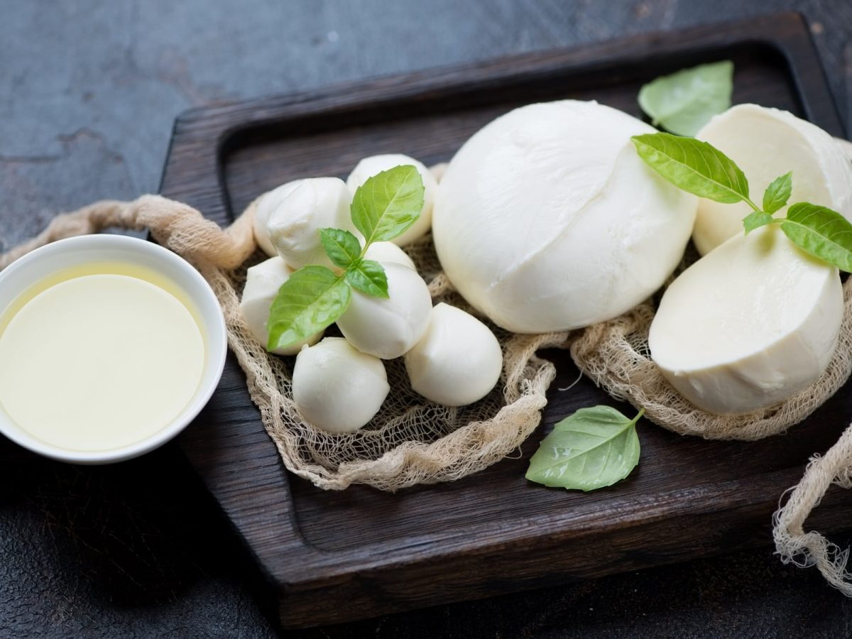 Mehrere Kugel Mozzarella liegen auf einem groben Tuch. daneben eine Schale mit Lake sowie Basilikumblätter.