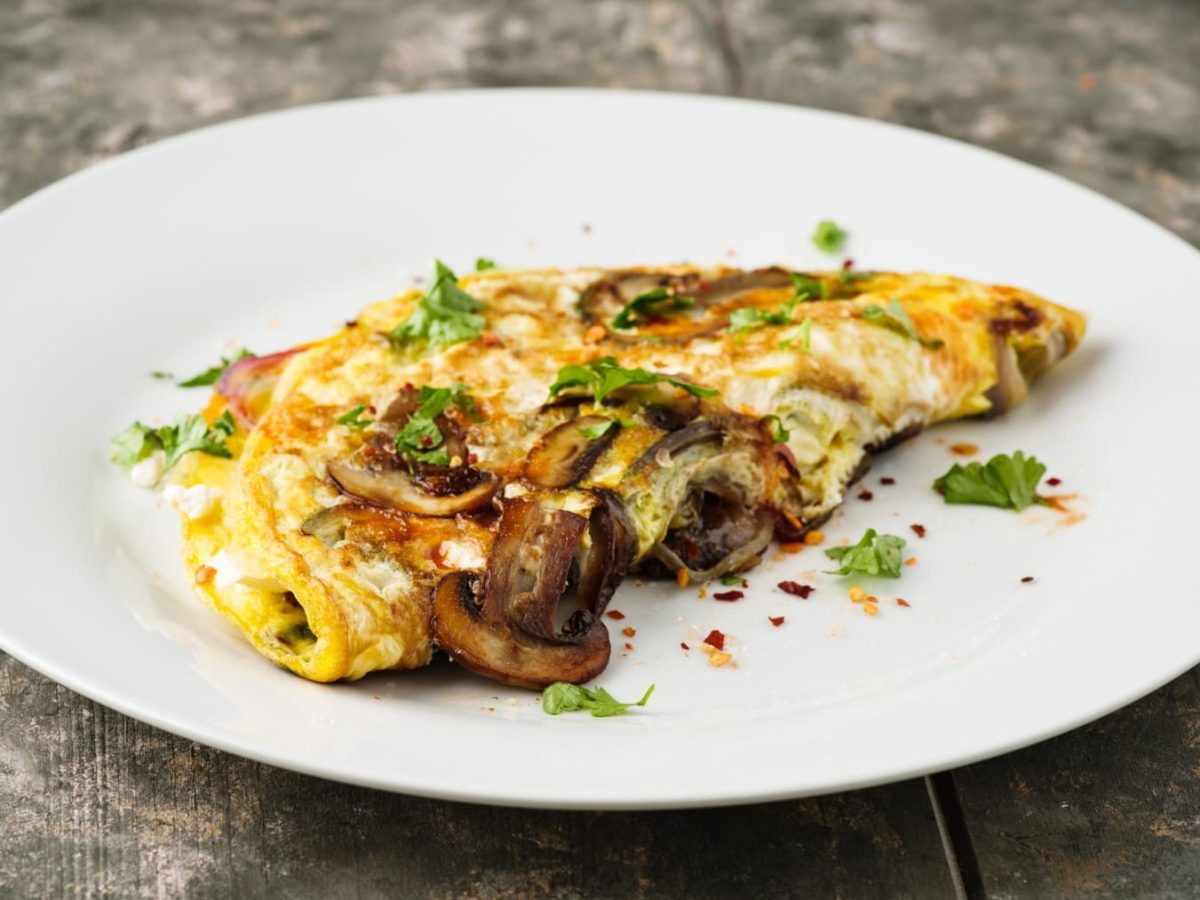 Omelett mit Champignons und Feta auf einem weißen Teller auf einem hölzernen Untergrund.