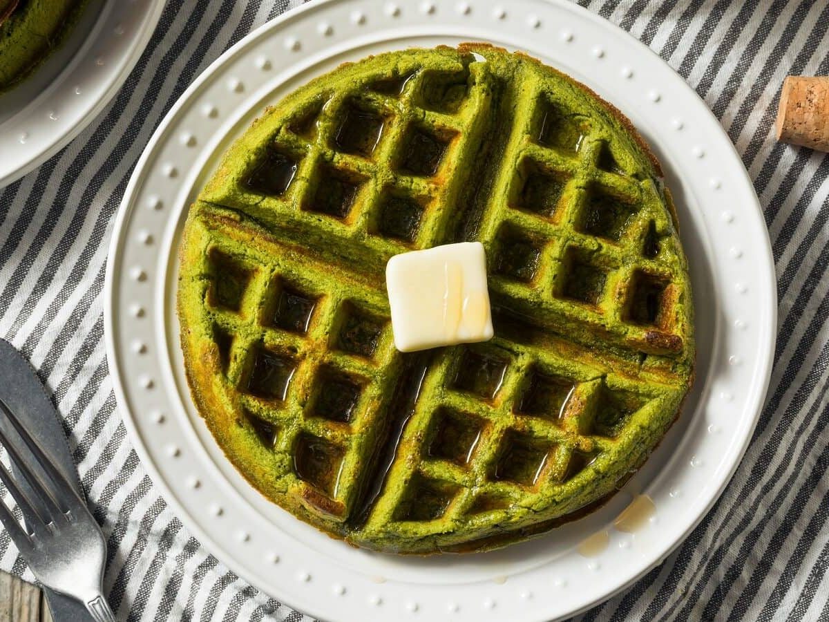 Pandan-Waffeln mit einem Stück Butter auf einem weißen Teller, der auf einem blau-weiß gestreiften Geschirrtuch liegt