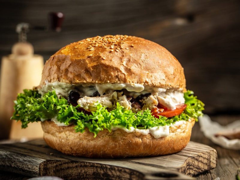 Pulled Chicken Burger auf einem Holzbrett. Im Hintergrund verschiedene Zutaten.