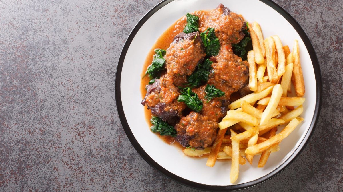 Rabo de Toro Cordoba spanischer Ochsenschwanz mit Spinat und Pommes auf Teller auf grauem Untergrund. Aufnahme aus der Vogelperspektive.