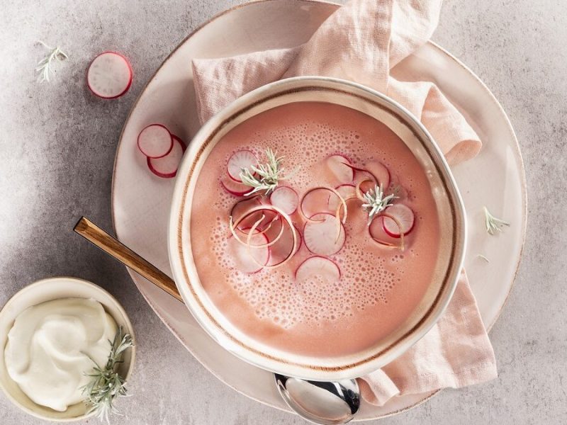 eine Schüssel mit einer Radieschen-Suppe mit Crème fraîche steht auf einem hellen Untergrund.