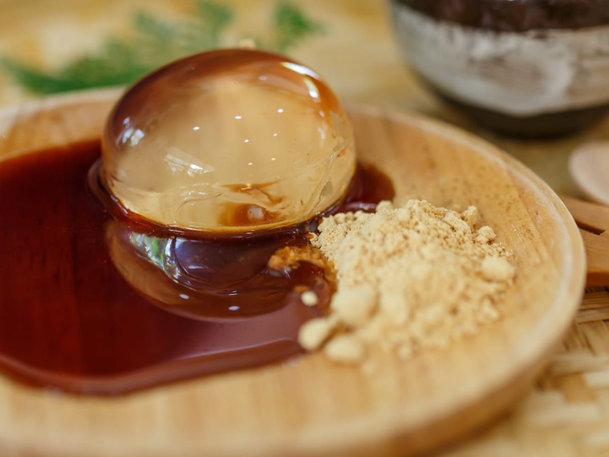 Aloe Vera Raindrop Cake mit Kokosblütensirup und geröstetem Sojamehl auf einer runden Holzplatte