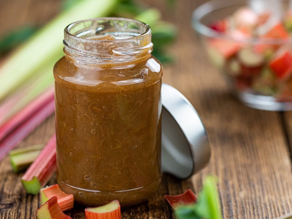 Rhabarber-Marmelade mit Banane und Vanille auf einem Holztisch. Daneben ist frischer Rhabarber.