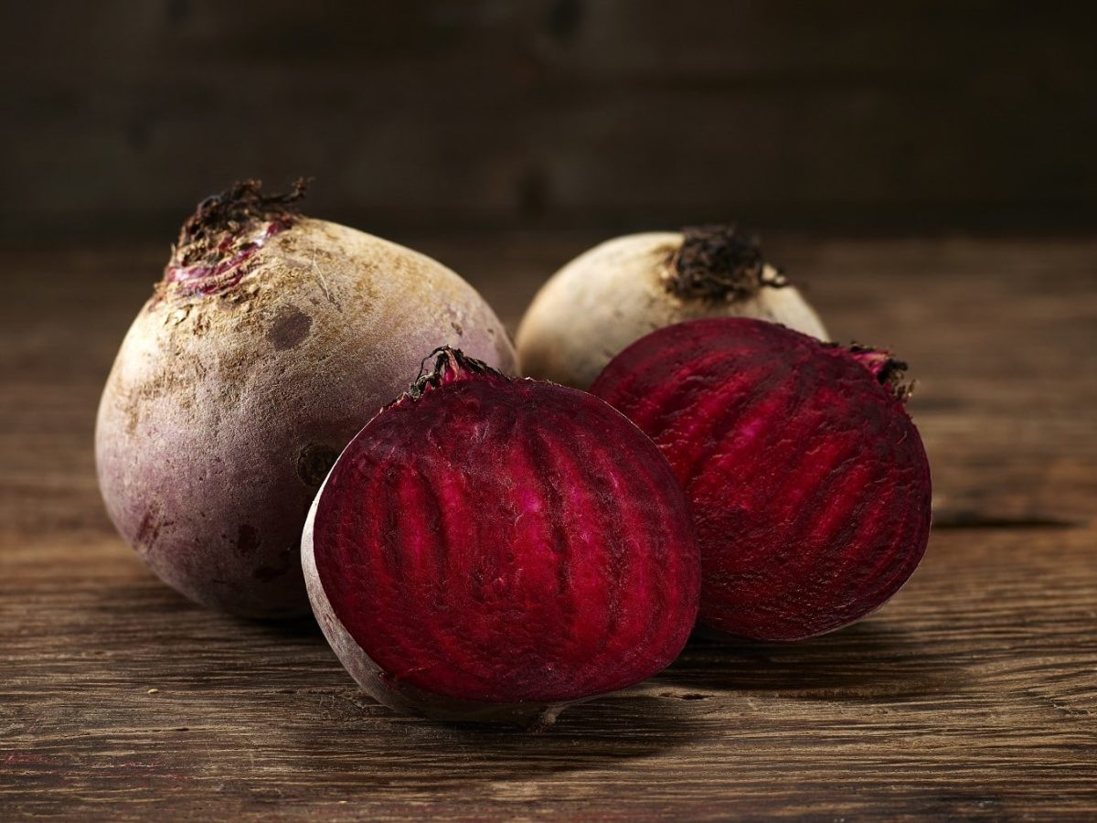 Rote Bete Roh essen: Frische Rote Bete, ungeschält und halbiert aufgeschnitten auf einem braunen Holztisch angerichtet.