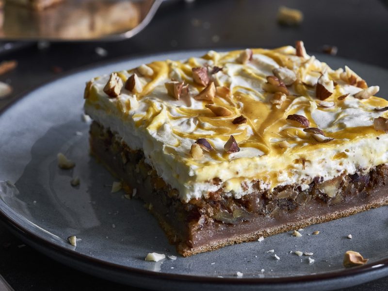 Schmandkuchen mit Karamellsauce auf einem grauen Teller. Daneben liegt eine Gabel.