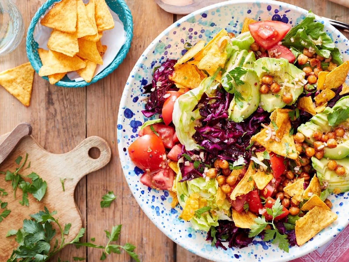 Eine Taco-Bowl in einem hellblau-weißen Teller auf einem Holztisch neben einem Holzschneidebrett und frischer Petersilie