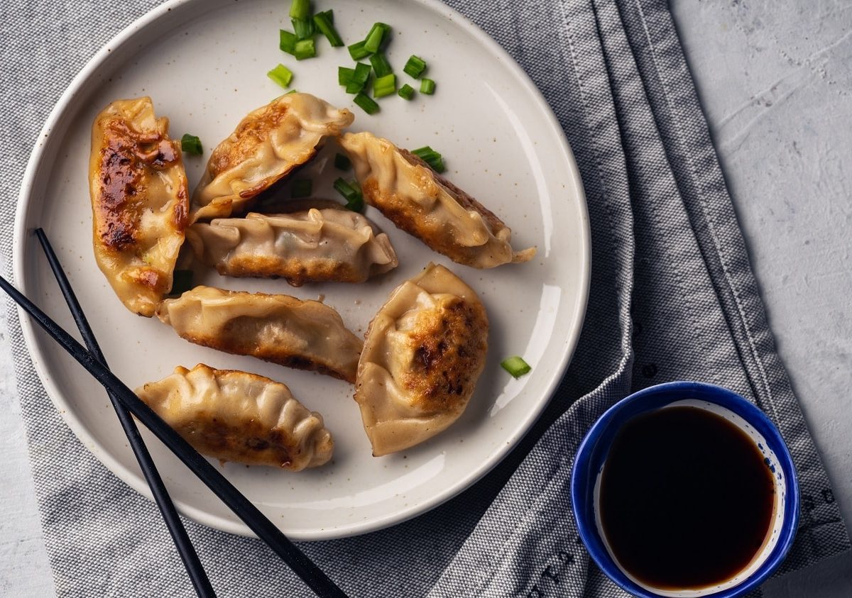 Tag der Gyoza mit ein paar Gyoza auf einem weißen Teller auf einem grauen Geschirrtuch und einem paar schwarzen Stäbchen