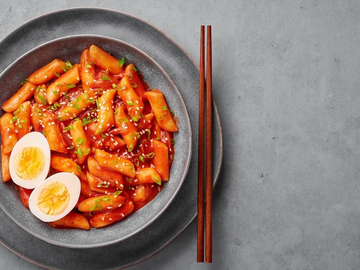 Eine Schüssel mit koreanischem Tteokbokki und einem Paar Stäbchen auf einem grauen Hintergrund.