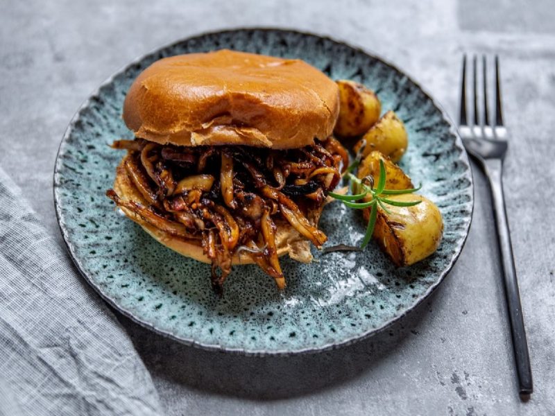 Veganes Pulled Pork aus Austernpilzen in einem Burger serviert auf einem blauen Teller.